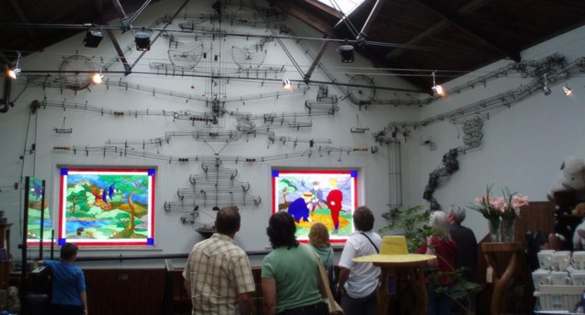 A marble run installation on a white wall in a museum, with visitors watching.