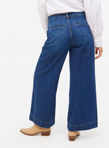 A model seen from the back wearing wide-leg blue jeans and beige ankle boots.