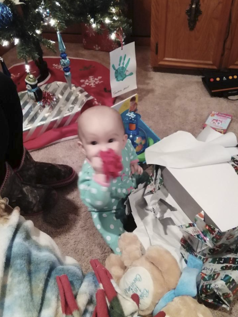 A baby in a polka-dot onesie playing with Christmas gifts.