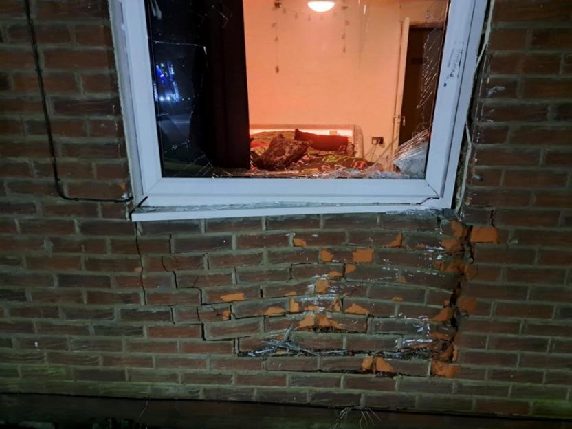 A window with shattered glass and a damaged brick wall below it.