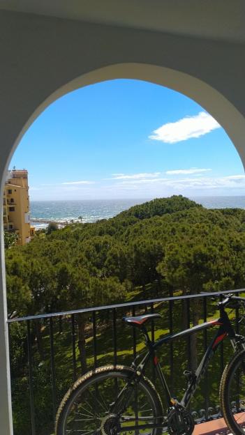 A mountain bike on a balcony overlooking a coastline with hills and the ocean.