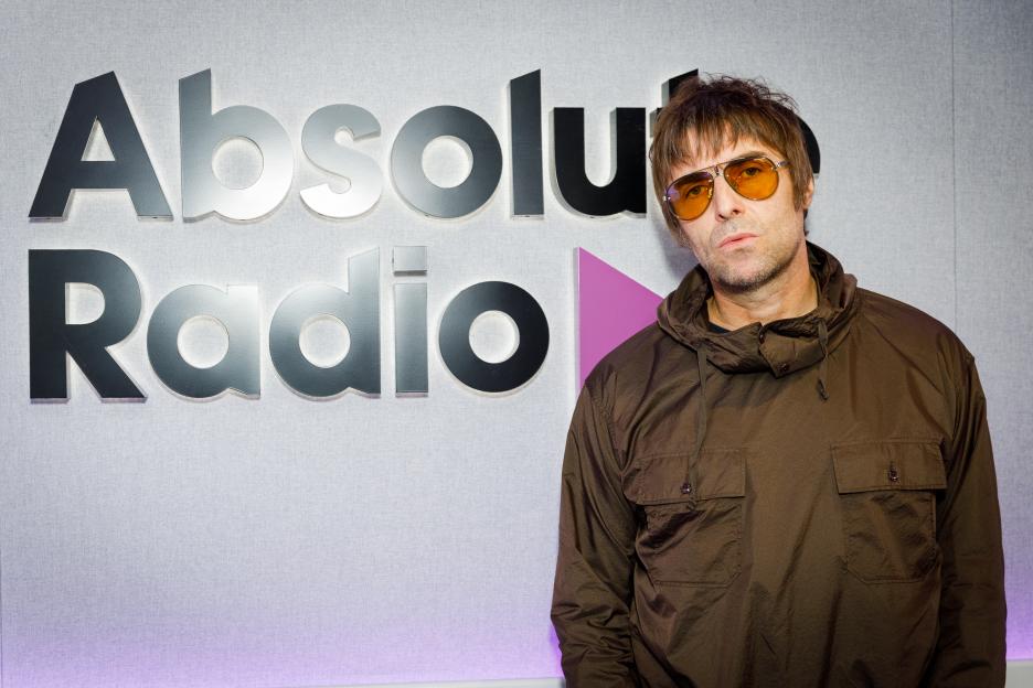 Liam Gallagher poses in front of an Absolute Radio sign.