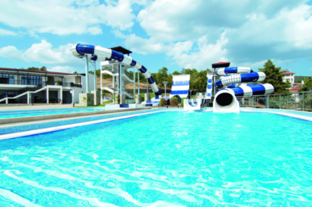 An outdoor pool with blue and white waterslides under a cloudy sky.