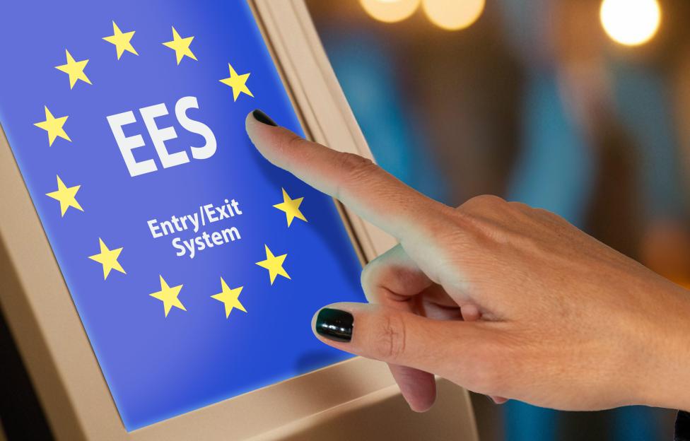 A woman's hand touching a screen with the EU flag and the text "EES Entry/Exit System".