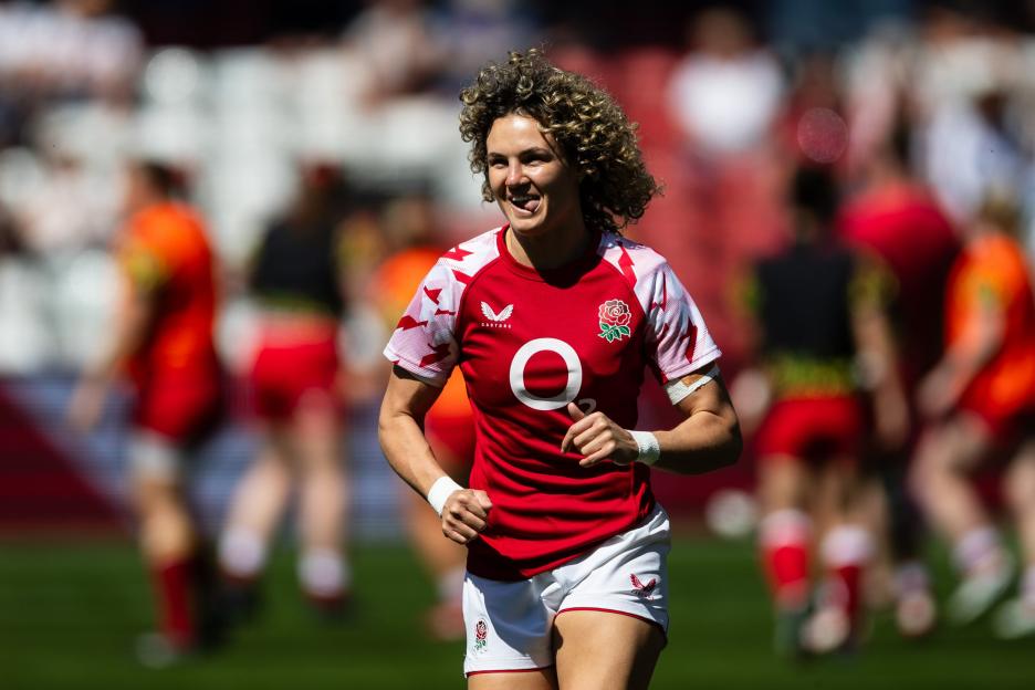 A female rugby player in a red England jersey runs and smiles during the Women's Six Nations match.