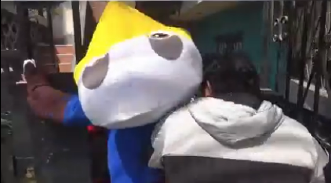 A person in a yellow, white, and blue mascot costume hitting a person in a white hoodie.