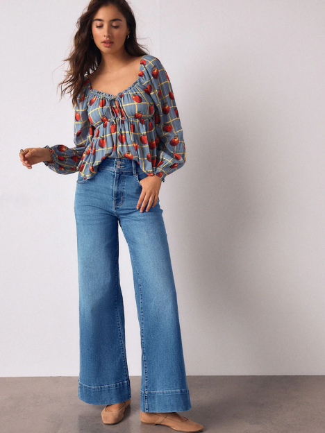 Woman wearing a blue top with red apple print and high-rise, wide-leg denim jeans.