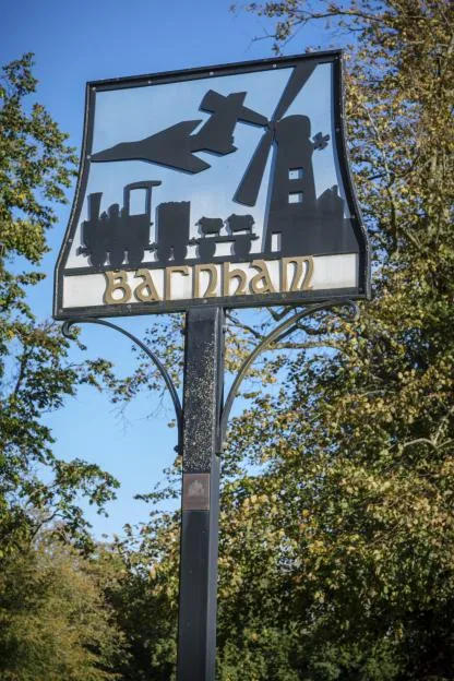 The village sign for Barnham in Suffolk, featuring silhouettes of a steam train, an airplane, sheep, and a windmill.