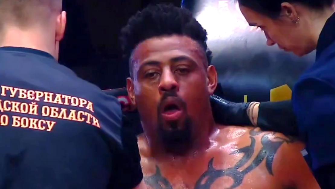 Greg Hardy exhausted, mouth open, with tattoos on his chest, while being tended to by two people in blue shirts.