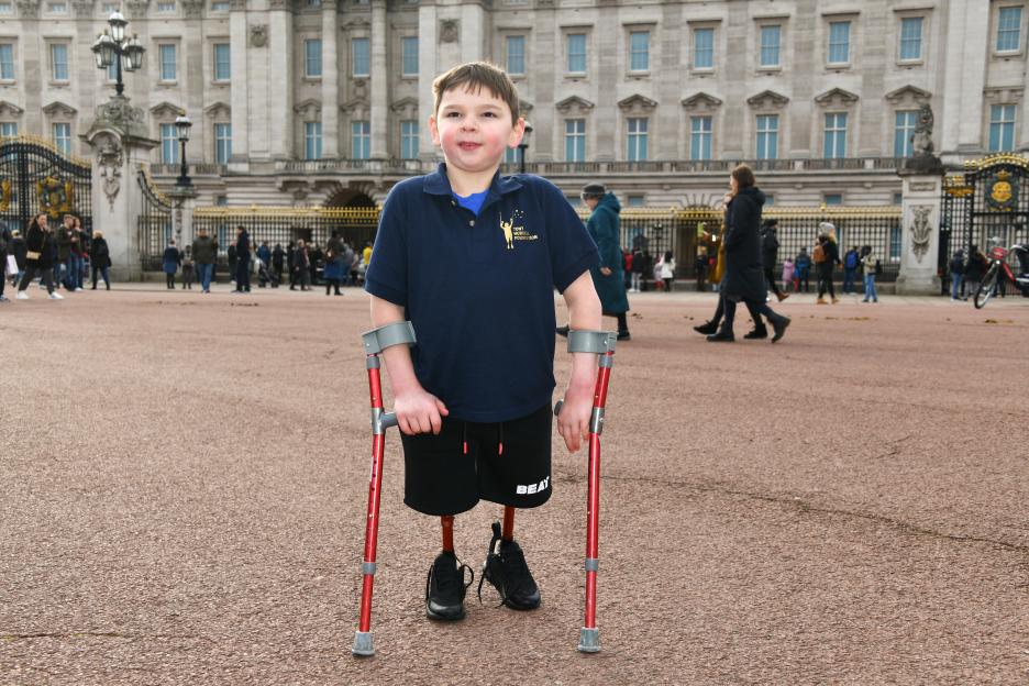 Tony Hudgell with crutches outside Buckingham Palace, celebrating fundraising efforts for his foundation.