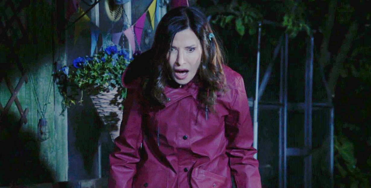 Bea in Eastenders looking surprised and distressed while wearing a red rain jacket.