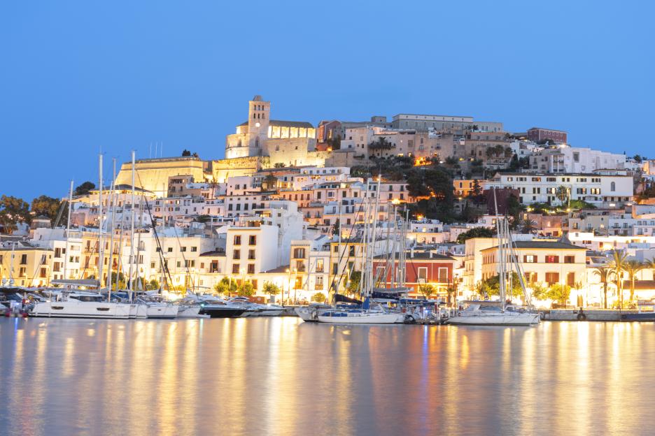 The old town of Ibiza, with its harbor full of boats and buildings illuminated at dusk.