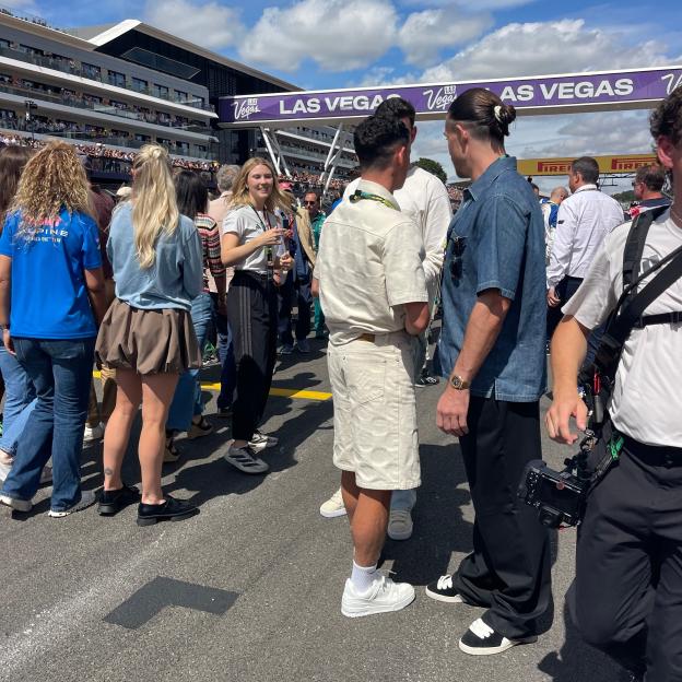 People gathered on an asphalt track with a "Las Vegas" sign overhead and spectators in a grandstand in the background.