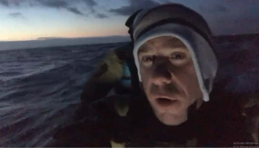 Man in a hat on a boat in choppy water at dusk.