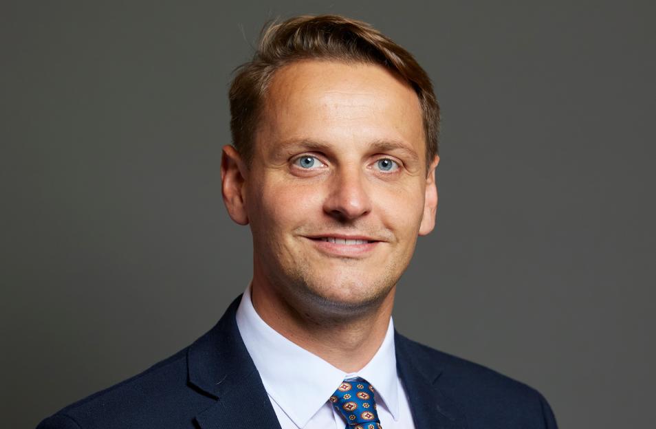 Mike Tapp, the immigration minister, stands in a dark suit and patterned tie.