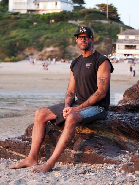 Chris Harding, owner of a coffee business on Polzeath Beach, sitting on rocks with the beach in the background.