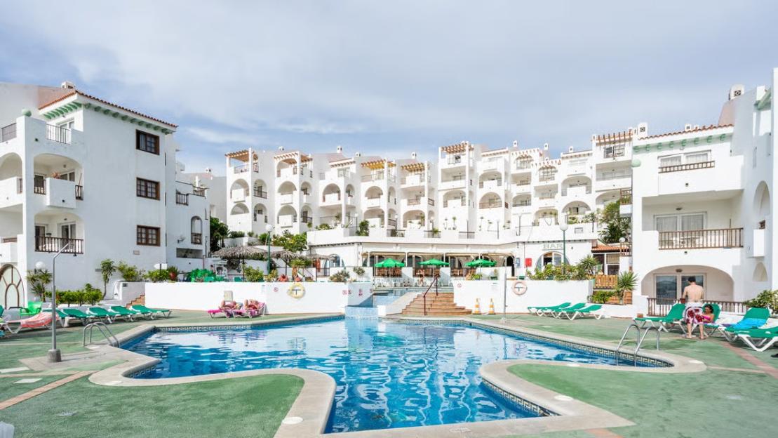 A resort with white buildings, balconies, and a swimming pool in the foreground.