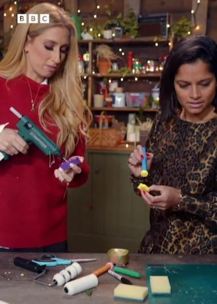 Two women crafting, with one holding a glue gun and the other holding a small blue stamp.
