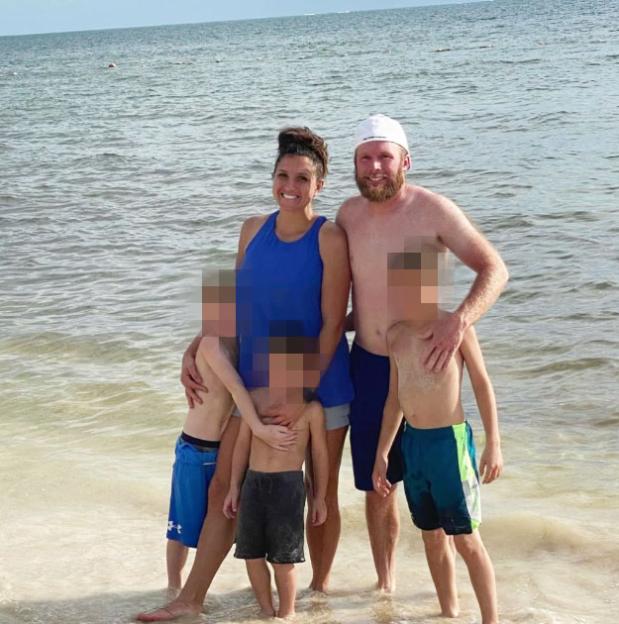 Family of five, with three children, standing in shallow ocean water.