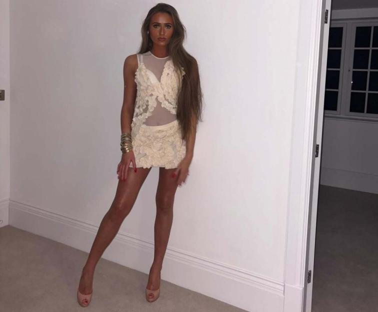 A young woman with long brown hair wears a cream-colored dress and high heels.