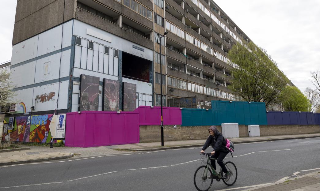 A person on a bike cycles past the Aylesbury Estate in Walworth, South London, with construction fencing and murals in the foreground.
