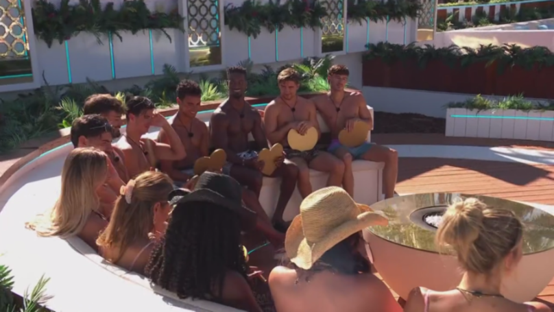 Men holding heart-shaped paddles face women in a hot tub.