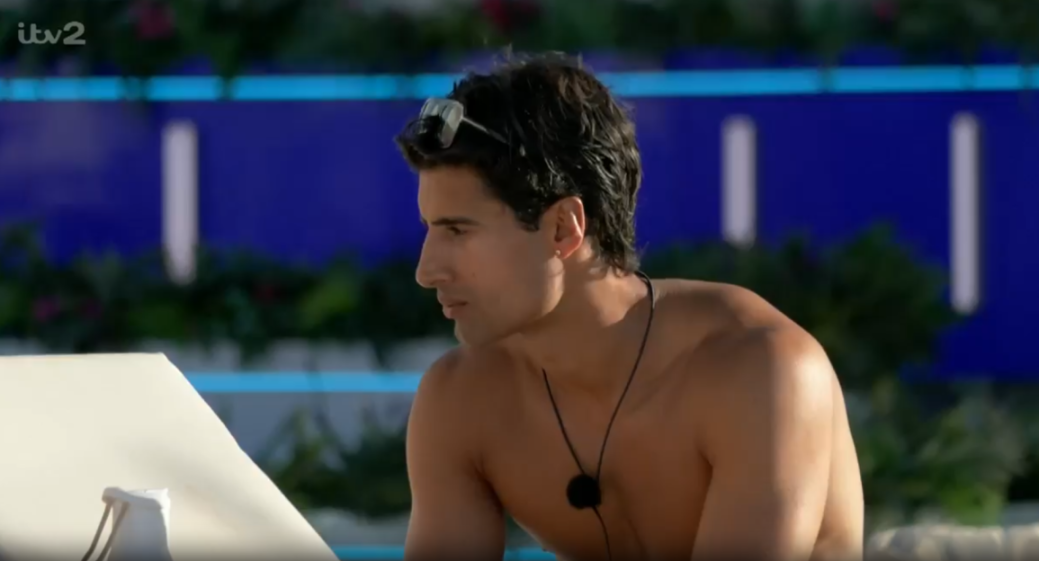 A shirtless man with sunglasses on his head looks at a white table.
