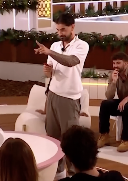 A man with dark hair and a white polo shirt points to his left while holding a red object.