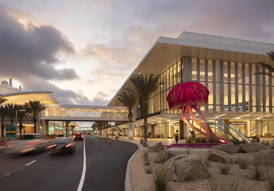 An outdoor view of a modern airport terminal with a large jellyfish sculpture and blurred vehicles driving by.