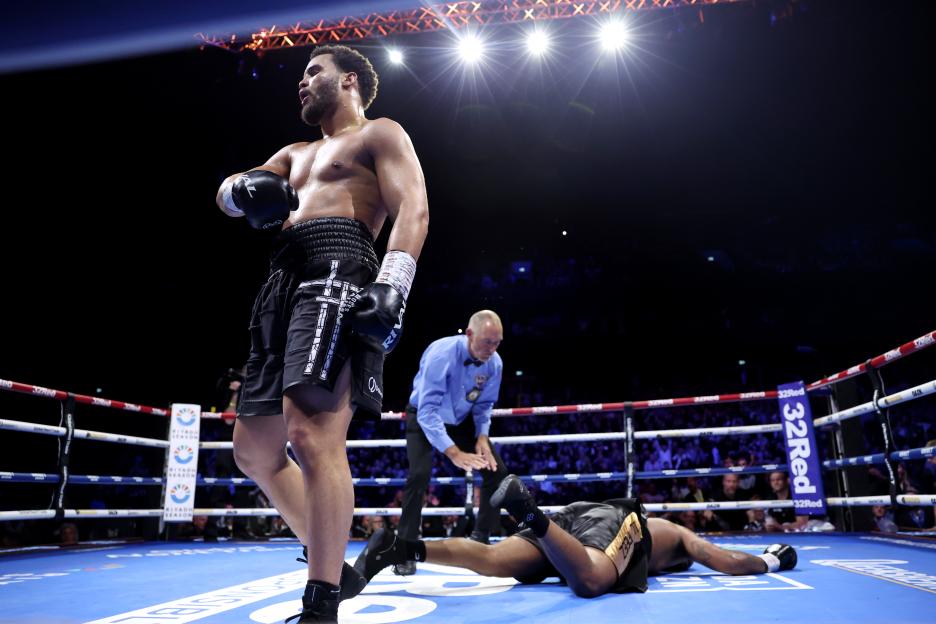 Moses Itauma standing in a boxing ring, with Jermaine Franklin Jr knocked out on the canvas and a referee looking down.