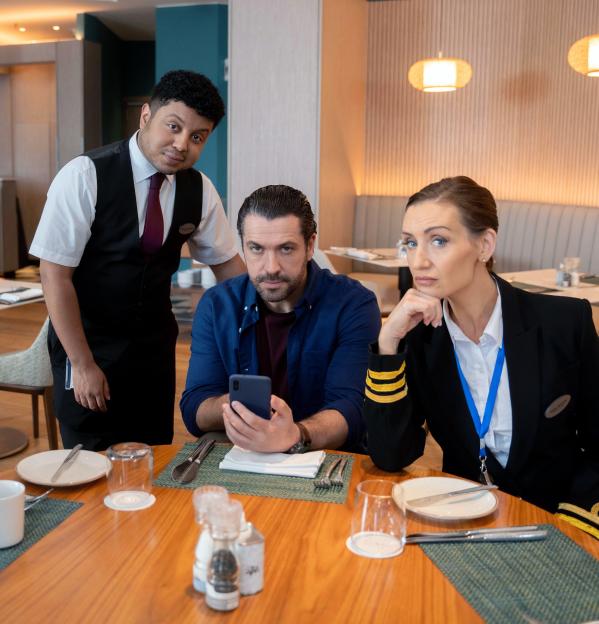 A restaurant staff member, a man, and a woman in a captain's uniform are seated at a wooden table.