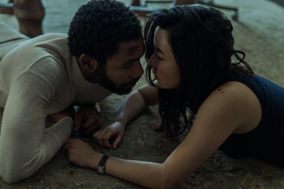 Donald Glover and Maya Erskine, as John and Jane Smith, lie on a patterned rug, looking at each other, their faces close.