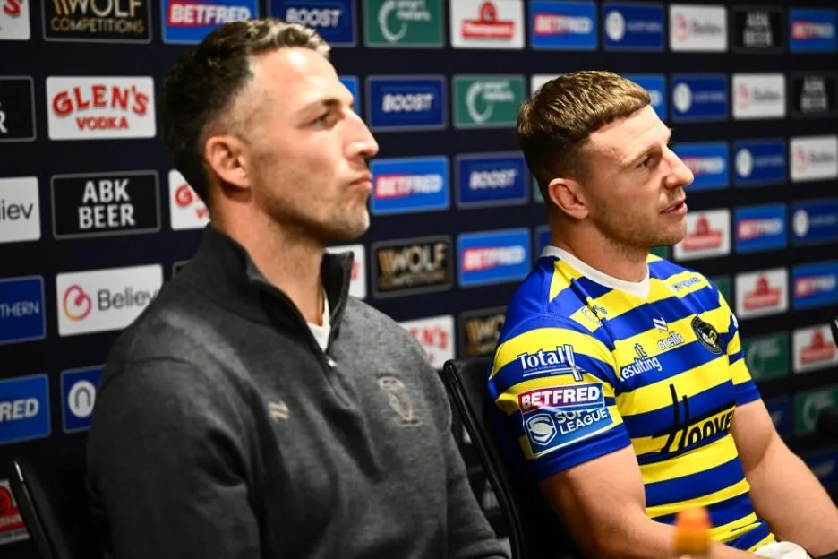 Sam Burgess and George Williams sitting in front of a sponsor backdrop.