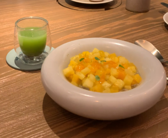 Chia pudding topped with mango and pineapple, next to a glass of green juice.