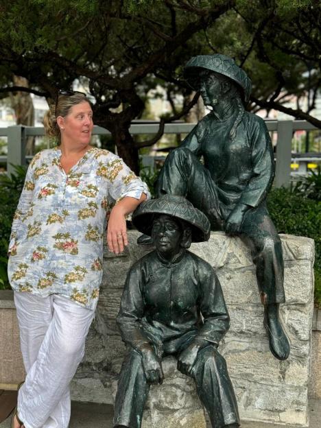 Shona Sibary standing next to two statues of people in traditional attire.