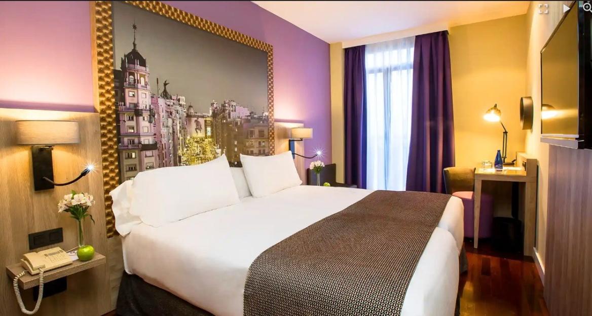 Hotel room with a large bed, purple and yellow walls, and a large print of a city above the headboard.