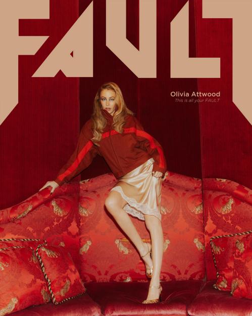 Olivia Attwood in Fault Magazine, wearing a reddish-brown jacket and a cream slip dress, posed on a red couch.