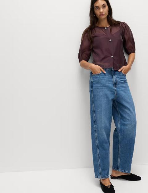 Model wearing a black organza top with embellished buttons and blue jeans.