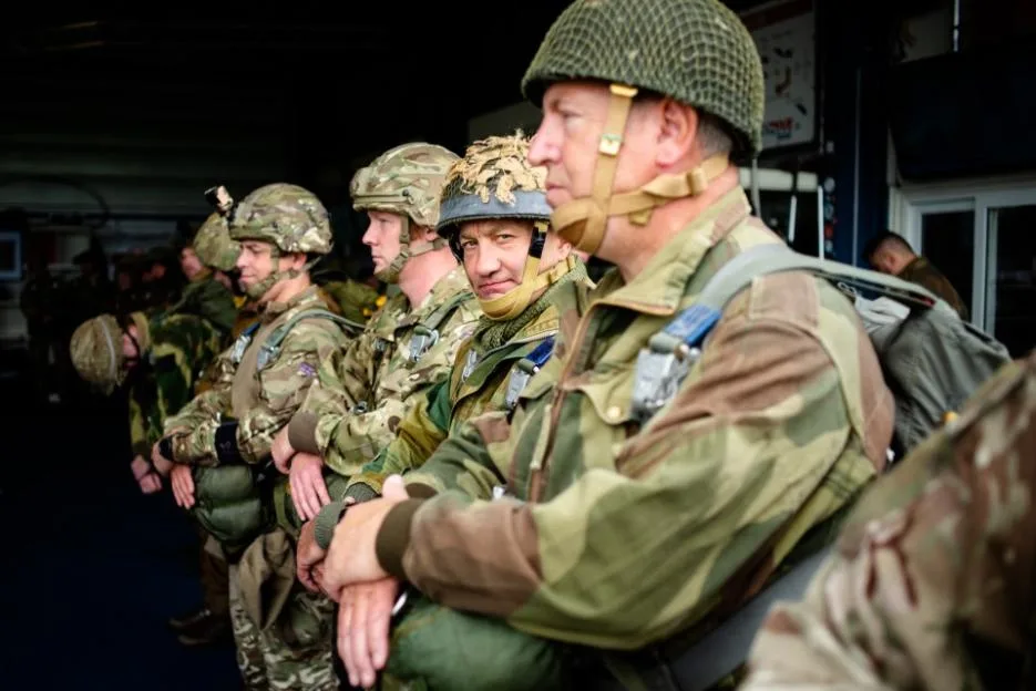 Soldiers, civilians, and veterans in military attire wait to board a plane before parachuting over Arnhem.