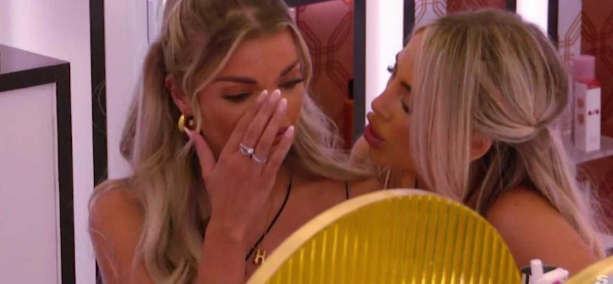 A woman crying with her hand over her face while another woman comforts her.