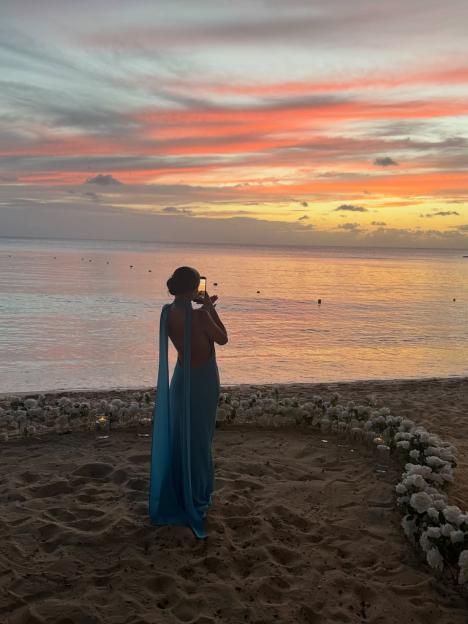 Love Island star Georgia Steel in a blue dress taking a photo of a sunset over the ocean.