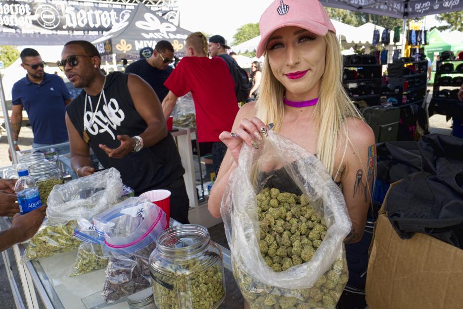A bud tender holding a large bag of cannabis at a High Times Cannabis Cup event.