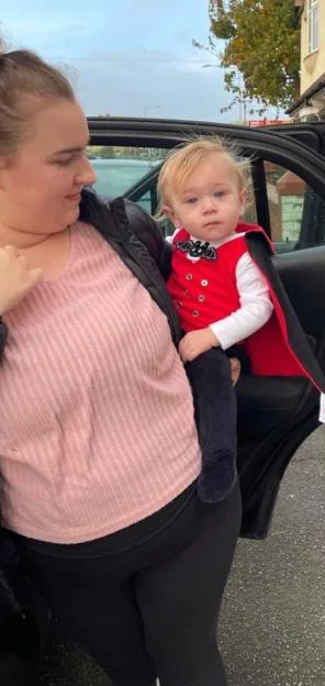 A woman holding a toddler dressed in a vampire costume by a car.