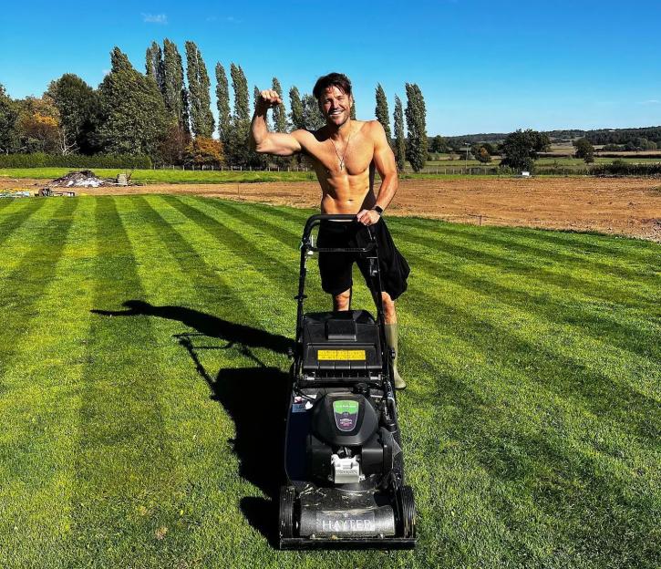 Mark Wright standing shirtless with a lawnmower on a striped lawn.