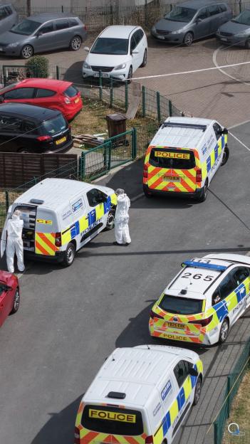 Overhead view of police vehicles and two people in hazmat suits at a crime scene.