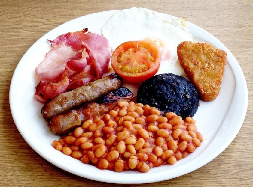 English breakfast with bacon, sausages, fried eggs, half a tomato, baked beans, a hash brown, and black pudding.