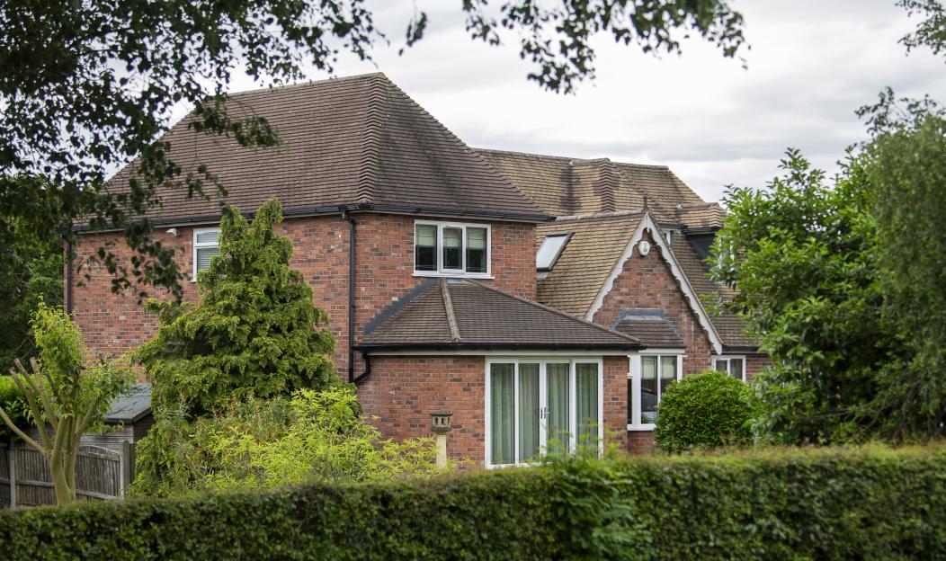 The former home of Andy Burnham in Culcheth, with red brick and a brown tiled roof, partially obscured by trees and a hedge.