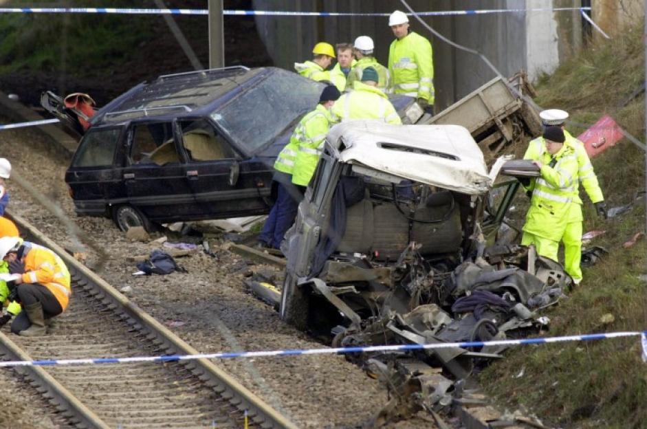Emergency personnel inspect the wreckage of two vehicles next to train tracks.