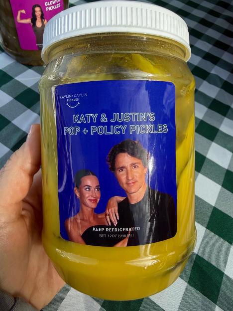 A hand holding a jar of "Katy & Justin's Pop + Policy Pickles" with photos of Katy Perry and Justin Trudeau on the label.