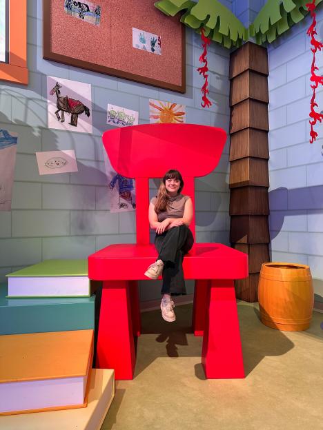 A woman poses sitting on a giant red chair in the new Pixar experience.
